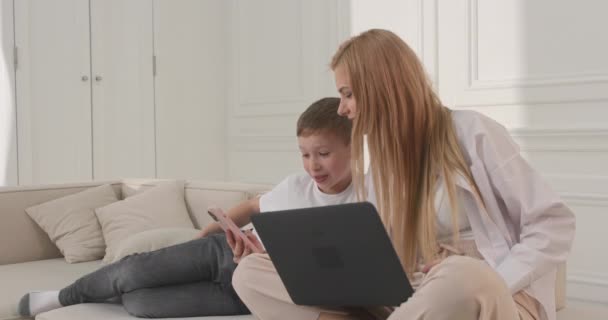 Mamá e hijo miran el teléfono sentado en el sofá. Mamá se ríe de un vídeo divertido. — Vídeos de Stock