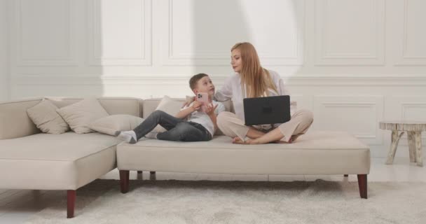 A srác vicces videókat mutat anyának a telefonban. Szórakozás anya és fia otthon. — Stock videók