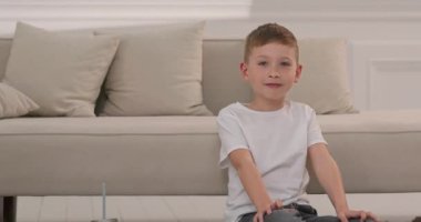 Yakışıklı çocuk yerde oturuyor ve kameraya gülümsüyor. Evdeki tatlı çocuk..
