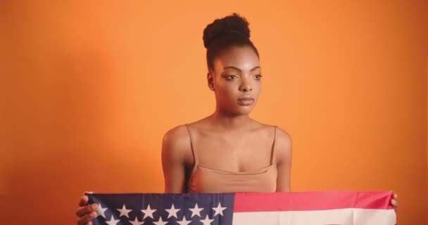 Ένα μαύρο κορίτσι κρατά τη σημαία της Αμερικής στα χέρια της και είναι λυπηρό. Κορίτσι με λυπημένες εκφράσεις προσώπου. — Αρχείο Βίντεο