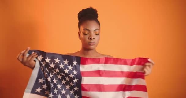 黒人の少女はアメリカの国旗を持っている。彼はそれを曲げ、それを細胞に投げ込む. — ストック動画