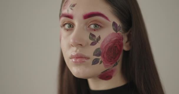 Крупним планом молода красива дівчина, чиє обличчя красиво пофарбоване квітами — стокове відео