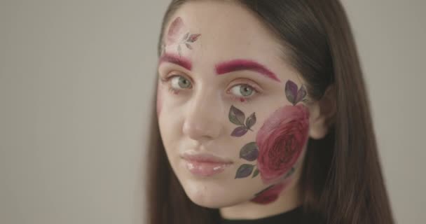 Πορτρέτο ενός όμορφου κοριτσιού με έντονα πράσινα μάτια που τονίζουν καθαρά τα ροζ λουλούδια στο πρόσωπό της — Αρχείο Βίντεο