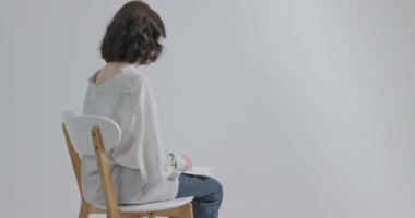 Genç, akranlarından farklı hissediyor. Kız beyaz arka planda bir sandalyede oturuyor..