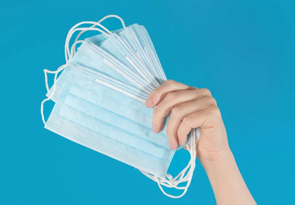 Hand holding up a fan of face masks, isolated against a bright blue background