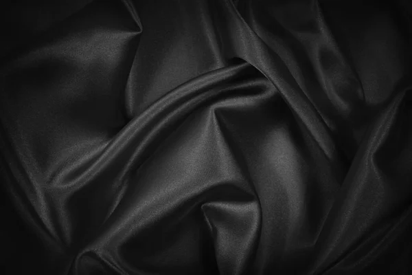 Black silk satin texture background. Beautiful wavy soft folds on shiny smooth fabric. Anniversary, event, card, invitation, concept. Black elegant background with copy space for design.