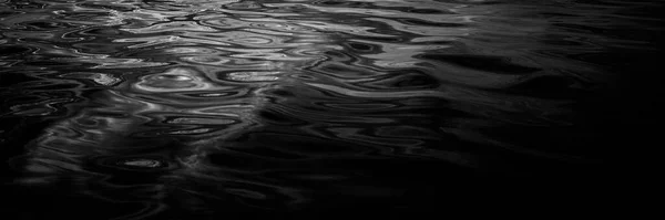 Black and white abstract background. Nightfall. Reflection of light on a wavy water surface. Ripples. Beautiful background with copy space for design. Web banner. Leaking, liquid, fluid, motion, wet.