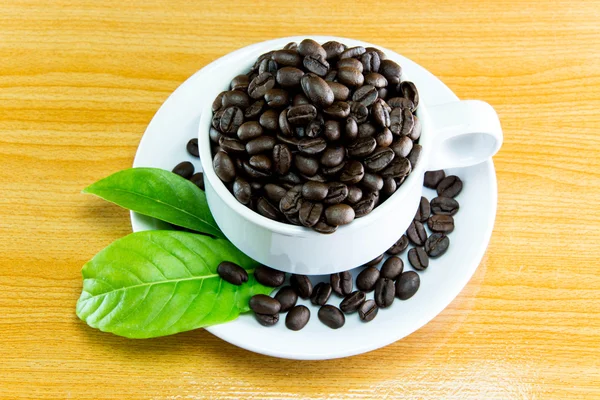 Stilleven kopje koffie bonen en bladeren koffie op houten tafel — Stockfoto