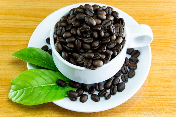 Stilleven kopje koffie bonen en bladeren koffie op houten tafel — Stockfoto