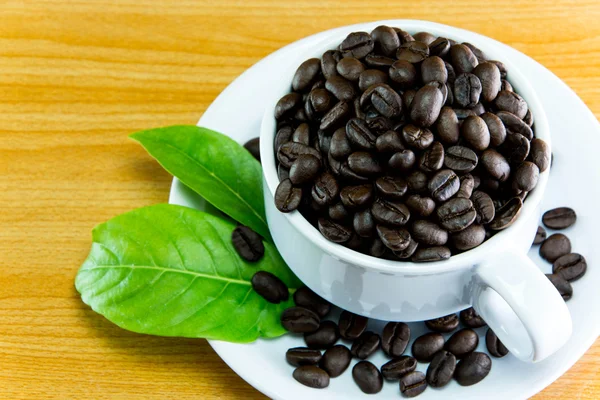 Stilleven kopje koffie bonen en bladeren koffie op houten tafel — Stockfoto