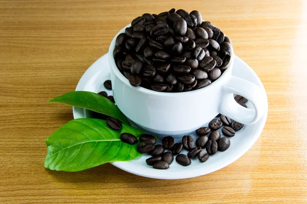 Zátiší pohár kávová zrna a listy kávy na dřevěný stůl — Stock fotografie