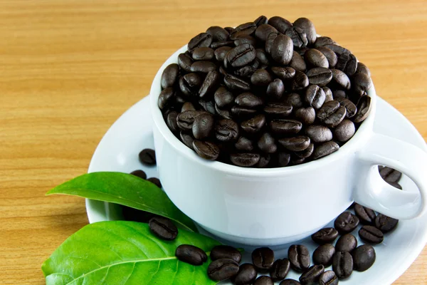 Stilleven kopje koffie bonen en bladeren koffie op houten tafel — Stockfoto