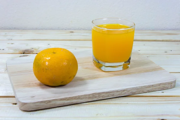 Glass of delicious orange juice and oranges on wooden table back — Stock Photo, Image