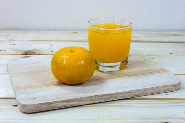 Glass of delicious orange juice and oranges on wooden table back — Stock Photo, Image