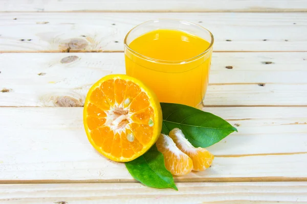 Copo de suco de laranja delicioso e fatias de laranja em t de madeira — Fotografia de Stock