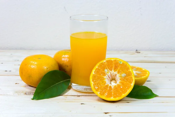Copo de suco de laranja delicioso e fatias de laranja em t de madeira — Fotografia de Stock