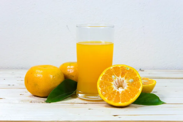 Copo de suco de laranja delicioso e fatias de laranja em t de madeira — Fotografia de Stock