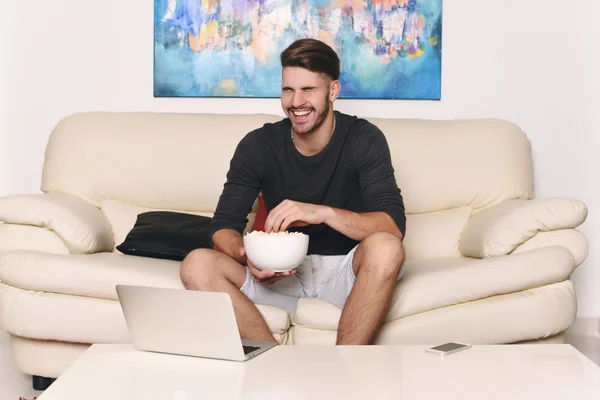 Joven comiendo palomitas de maíz y usando laptop — Foto de Stock