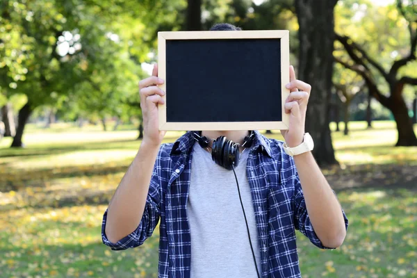 Young man with black headphones holding chalkboard . — Stock Photo, Image