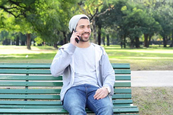 Giovane che parla al telefono seduto sulla panchina del parco . — Foto Stock