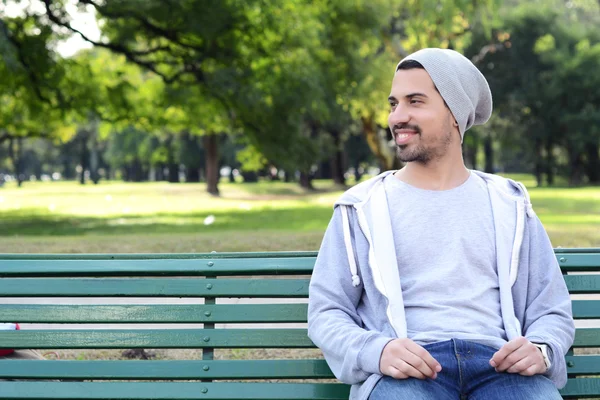 Jeune homme latin assis sur le banc du parc . — Photo