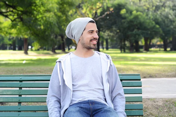 Giovane uomo latino seduto sulla panchina del parco . — Foto Stock