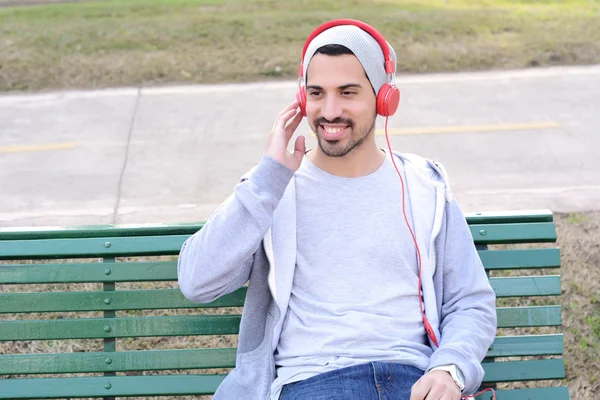 Joven escuchando música con auriculares sentados en el parque Ben —  Fotos de Stock