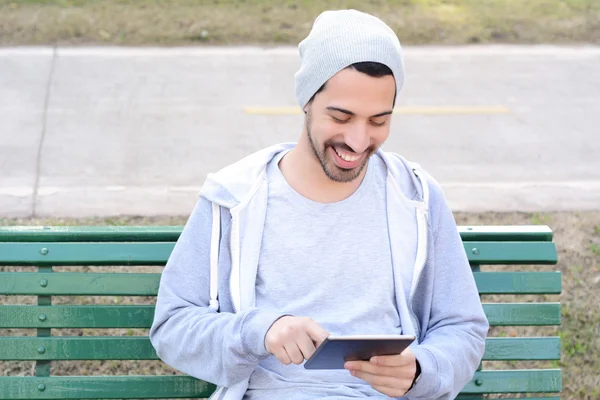 Mladý muž pomocí tabletu sedí na lavičce v parku. — Stock fotografie