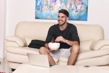 Patlamış mısır yemek ve dizüstü bilgisayar kullanarak bir genç adam