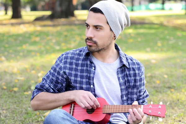 Jeune homme jouant de l'ukelele dans un parc . — Photo