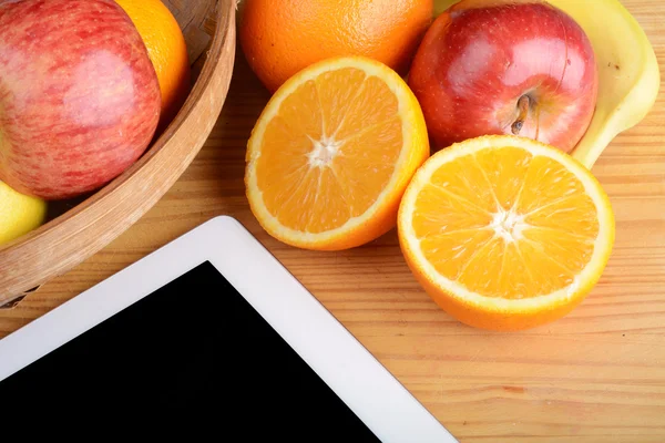 Fruits and a Tablet PC on wooden table.