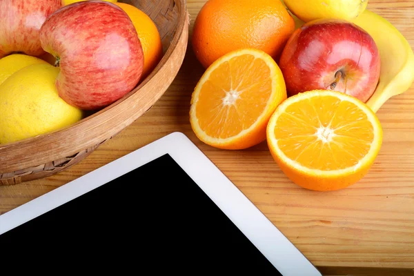 Frutas y un Tablet PC en mesa de madera . — Foto de Stock