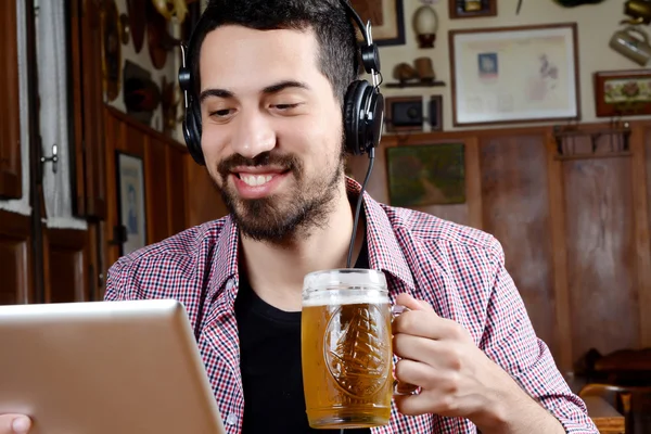 Чоловік п'є пиво з навушниками та цифровим планшетом . — стокове фото