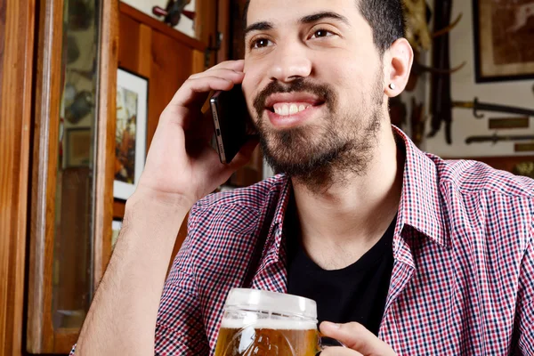 Latin man talking on the phone with glass of beer and snacks. — Stock Photo, Image