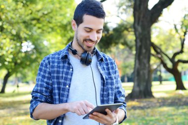 Genç adam parkta kulaklıklarla tablet kullanma.
