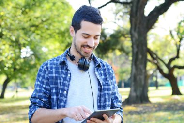 Genç adam parkta kulaklıklarla tablet kullanma.