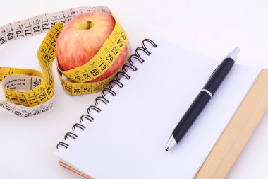 Bir elma ve not defteri üzerinde ölçüm bandı.