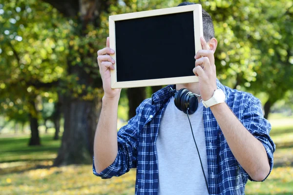 Young man with black headphones holding chalkboard . — Stock Photo, Image