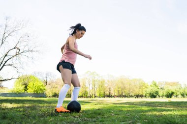 Genç bayan futbolcunun portresi sahada top oynarken koni etrafında koşuyor. Spor konsepti.
