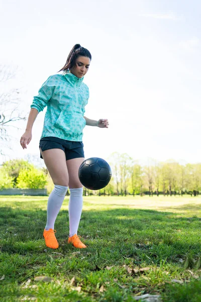 Portrait of young woman practicing soccer skills and doing tricks with the football ball. Soccer player juggling the ball. Sports concept.