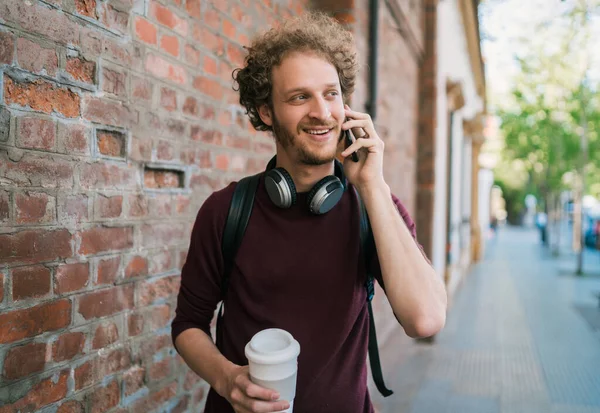 Portrait of young man talking on the phone while walking outdoors in the street. Communication and urban concept.