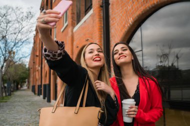 Sokakta cep telefonuyla selfie çeken iki genç arkadaşın portresi. Yaşam tarzı ve arkadaşlık kavramları.