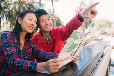Asyalı mutlu bir gezgin çiftin portresi. Elinde harita var ve yol tarifi arıyorlar. Seyahat ve tatil konsepti.