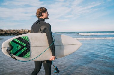 Genç sörfçü siyah sörf takımıyla okyanusta duruyor. Spor ve su sporları konsepti.