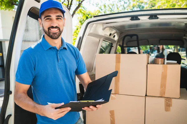 Portrait of a delivery man checking the products in checklist while standing right next to his van. Delivery and shipping concept.