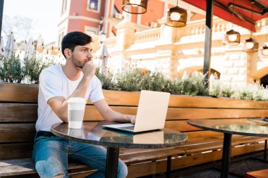 Genç adam bir kafede dizüstü bilgisayarını kullanıyor..