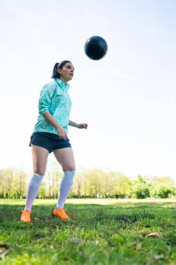 Genç bir kadın topla futbol oynuyor..