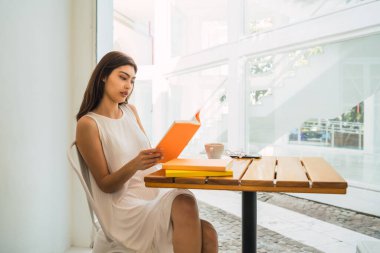 Kahve dükkanında kitap okuyan genç bir kadın..