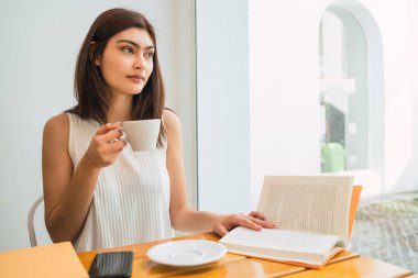 Genç bir kadın kahve dükkanında bir fincan kahve içiyor..