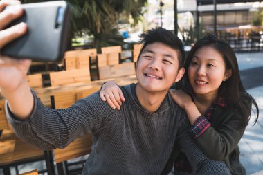Asyalı çift cep telefonuyla selfie çekiyor..